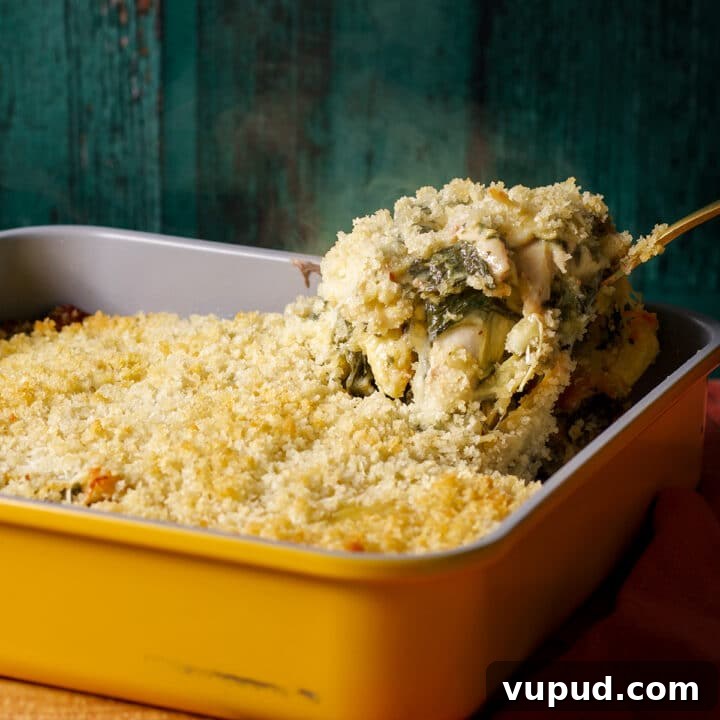 Someone using a large spoon to serve spinach artichoke chicken casserole.