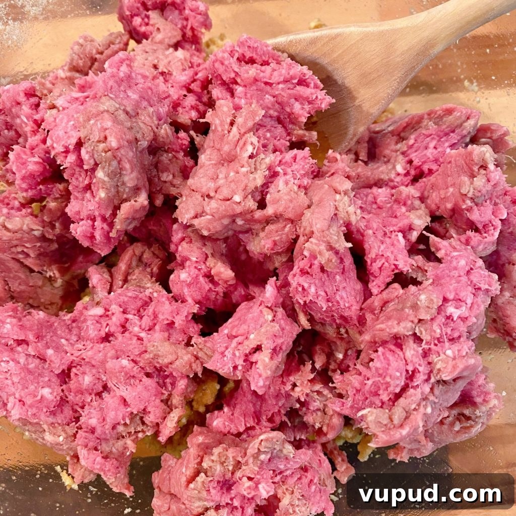 Cheesy Meatball and Hash Brown Casserole Recipe 4 Crumbled Ground Beef over meatball ingredients in a large glass bowl.