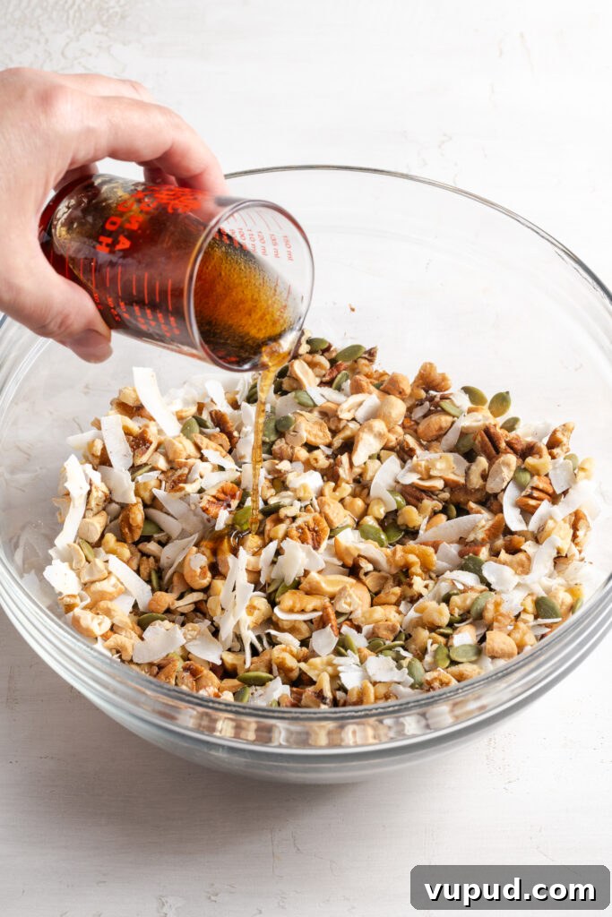 Grain-Free Homemade Granola Recipe for Crunchy, Low-Carb Mornings 8 action shot of hand pouring the liquid ingredients over the dry grain free granola mixture.