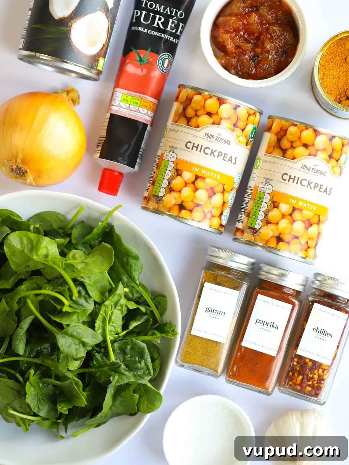 Slow-Cooked Chickpea and Spinach Curry (Chana Saag) 4 Ingredients including spinach, spices, chickpeas, tomato puree and a lemon laid on a counter.