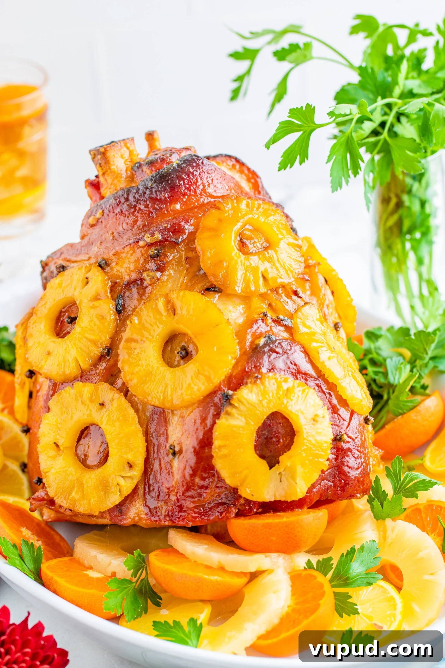 Glazed Pineapple Baked Ham Recipe for Holiday Dinner 2 Pineapple Baked Ham covered in pineapple on a large white dish with oranges and pineapple slices lining the bottom.