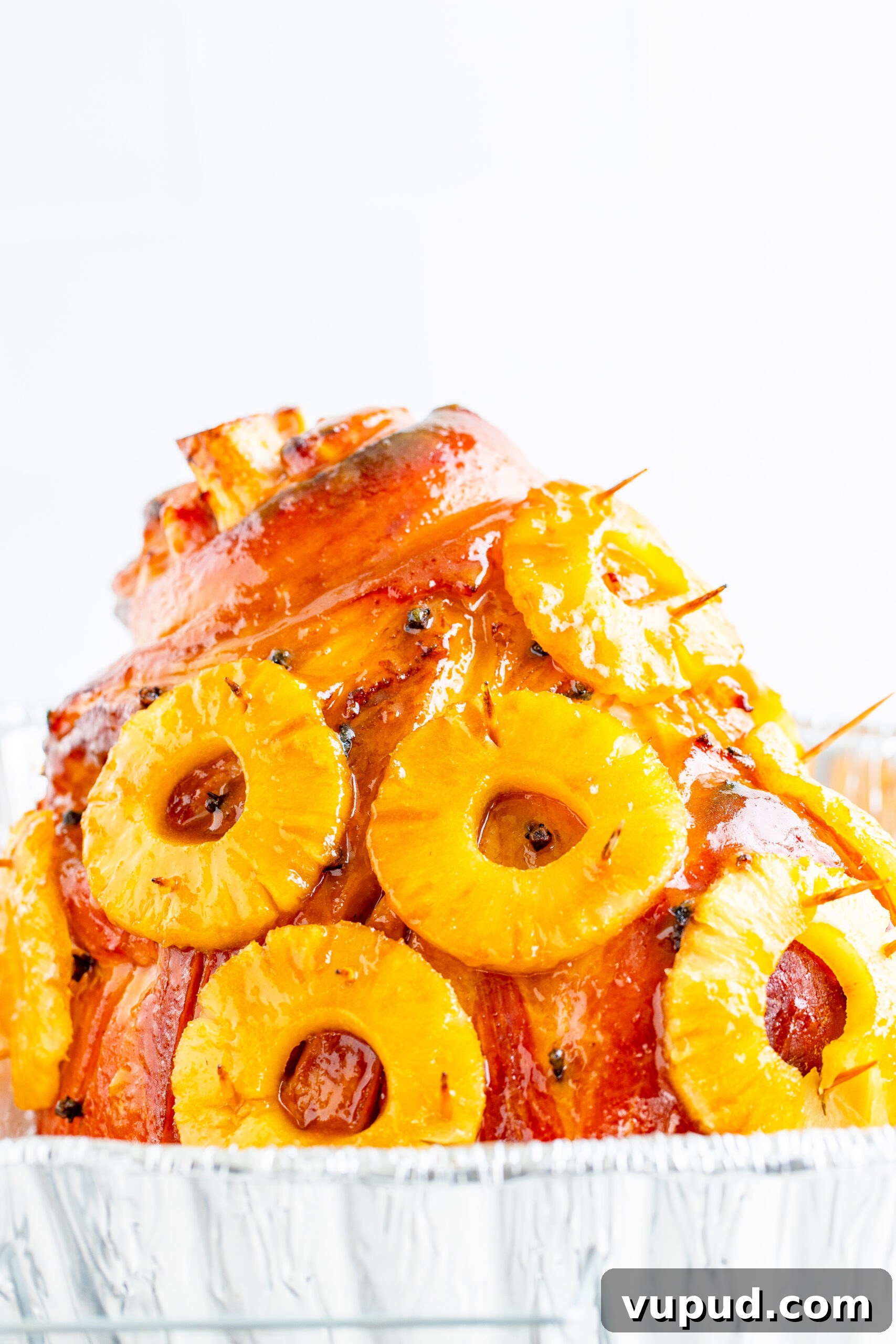 Glazed Pineapple Baked Ham Recipe for Holiday Dinner 11 Pineapple Baked Ham covered in pineapple on a large white dish with oranges and pineapple slices lining the bottom.