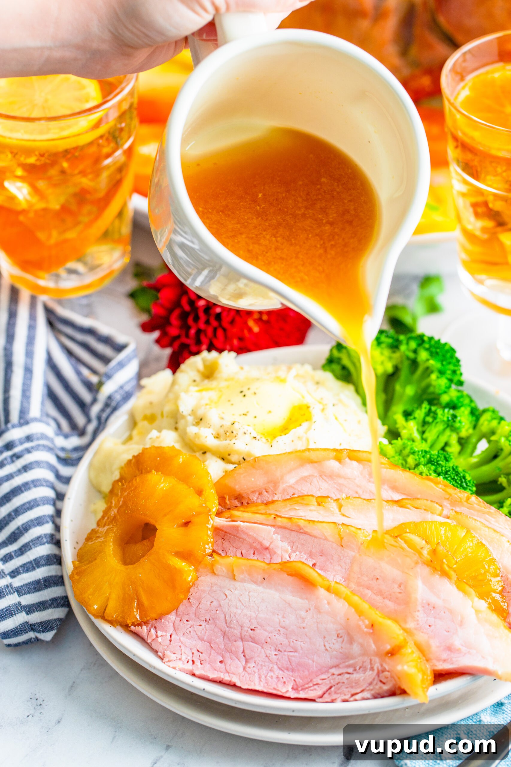 Glazed Pineapple Baked Ham Recipe for Holiday Dinner 12 pouring gravy over top the sliced and plated pineapple baked ham.