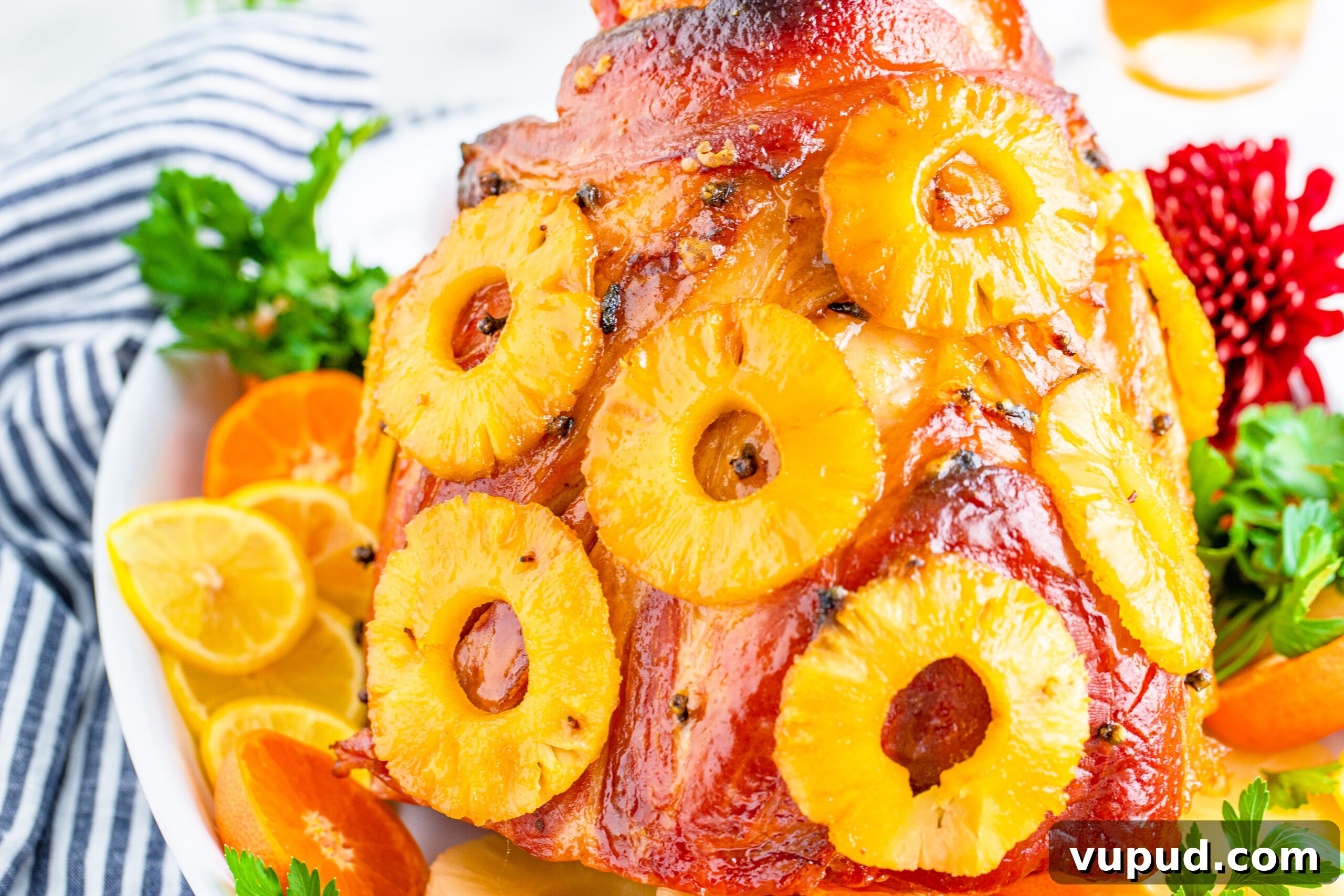 Glazed Pineapple Baked Ham Recipe for Holiday Dinner 10 Pineapple Baked Ham covered in pineapple on a large white dish with oranges and pineapple slices lining the bottom.