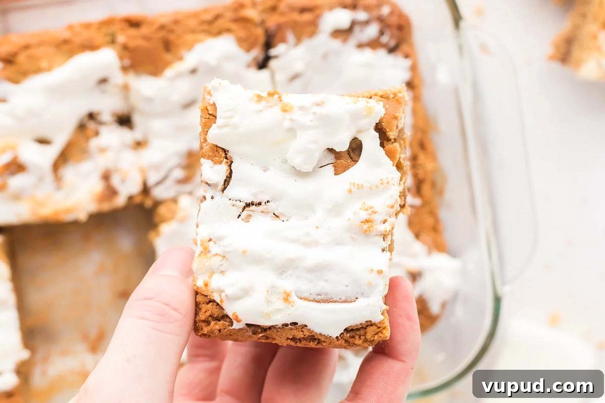 24 Irresistible S'mores Recipes to Enjoy All Year Long 5 A hand holding a s'mores bar with a bite taken out of it, revealing the layers and tempting S'mores Recipes with more bars in the background.
