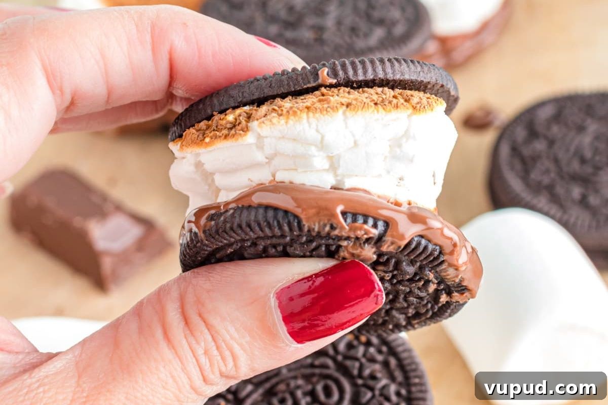 24 Irresistible S'mores Recipes to Enjoy All Year Long 8 A hand with a red manicure holding an oreo cookie s'more from our S'mores Recipes with a melted marshmallow and chocolate filling.