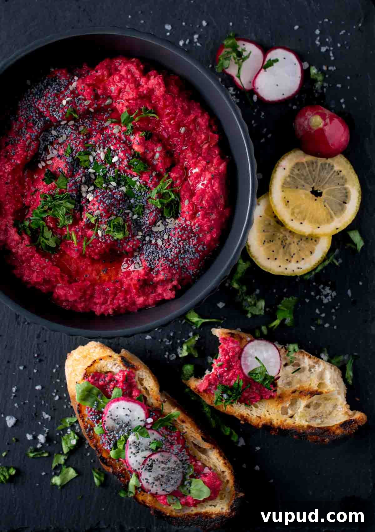 Vibrant Beetroot Hummus Recipe for Bright, Creamy Dip 2 Beetroot hummus in a black bowl with toasted bread and lemon slices on the side.
