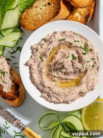 A bowl of tuna pate surrounded by toasted baguette, cucumber ribbons and lettuce.