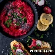Vibrant Beetroot Hummus Recipe for Bright, Creamy Dip 8 Beetroot hummus in a black bowl with toasted bread and lemon slices on the side.