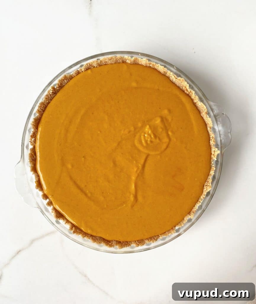 Pumpkin Pie with Graham Cracker Crust Recipe for Fall Baking 11 White marble surface with unbaked pumpkin pie on a glass dish.