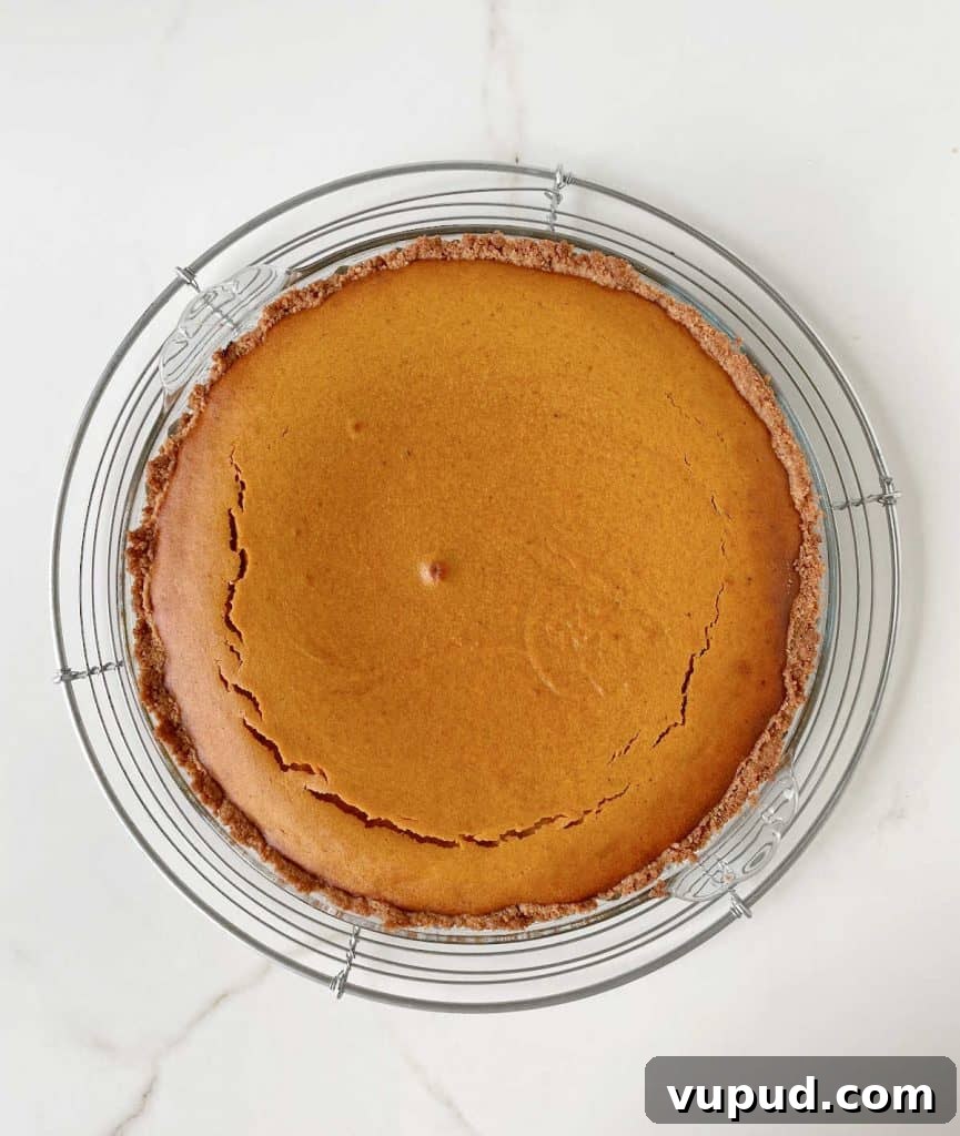Pumpkin Pie with Graham Cracker Crust Recipe for Fall Baking 12 Baked pumpkin pie on a glass plate on a wire rack. Top view on white marble surface.