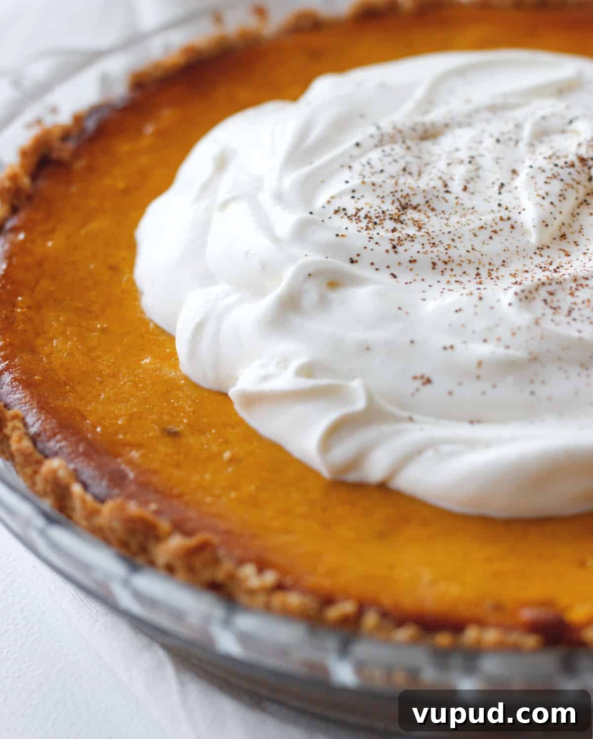 Pumpkin Pie with Graham Cracker Crust Recipe for Fall Baking 14 Partial view of a whole pumpkin pie topped with whipped cream.