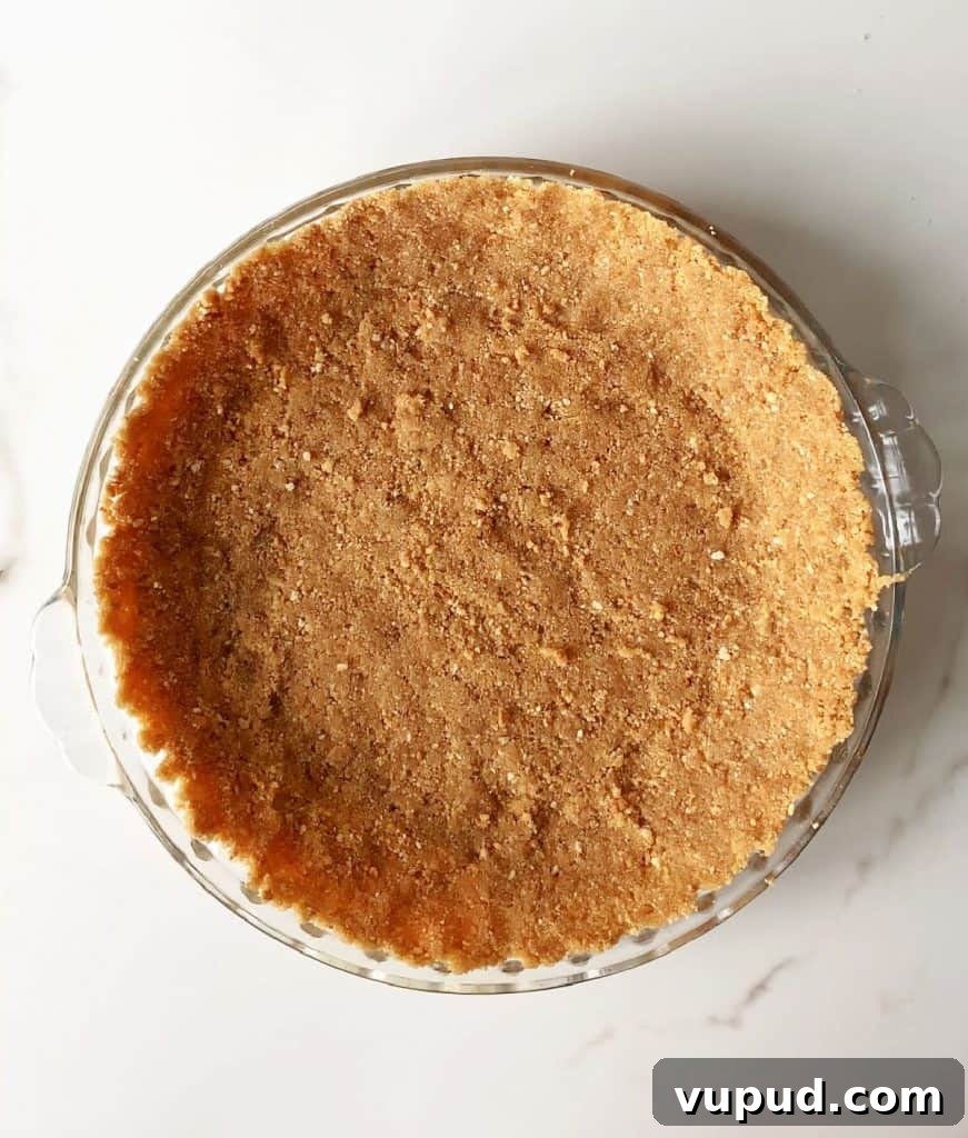 Pumpkin Pie with Graham Cracker Crust Recipe for Fall Baking 7 Graham cracker crust in a glass pie dish on a white marble surface. Top view.