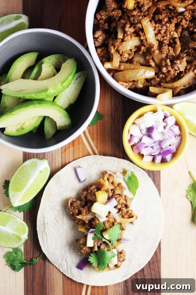 Overhead view of a ground beef taco, al pastor style with avocado and chopped red onion on the side