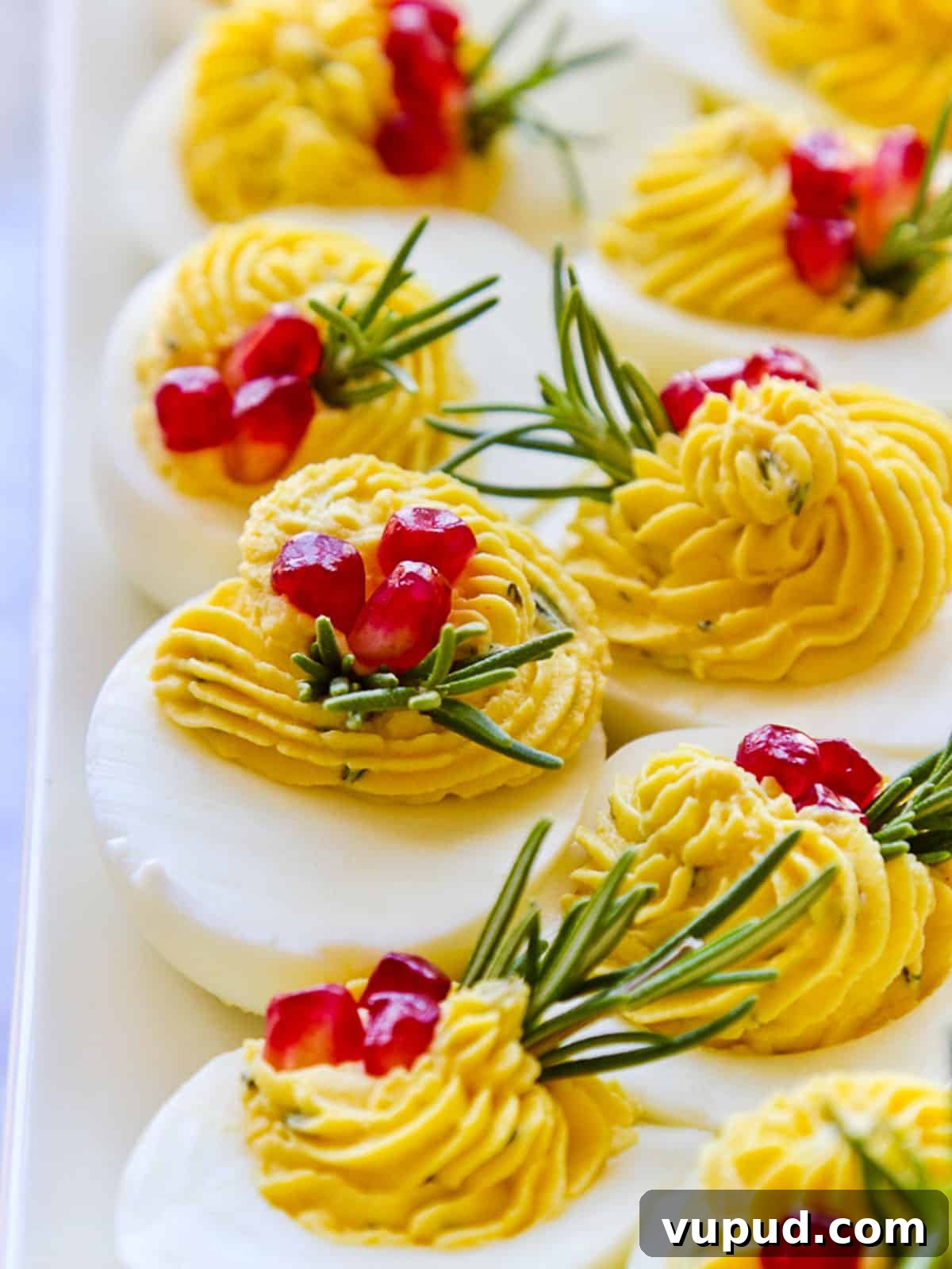 Festive Christmas Deviled Eggs Recipe for Holiday Parties 11 A platter of holiday Christmas deviled eggs garnished with rosemary and pomegranate seeds.