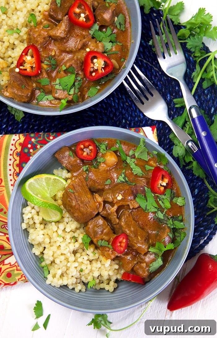 Overhead shot of thai red curry beef on a bed of couscous with a lime.