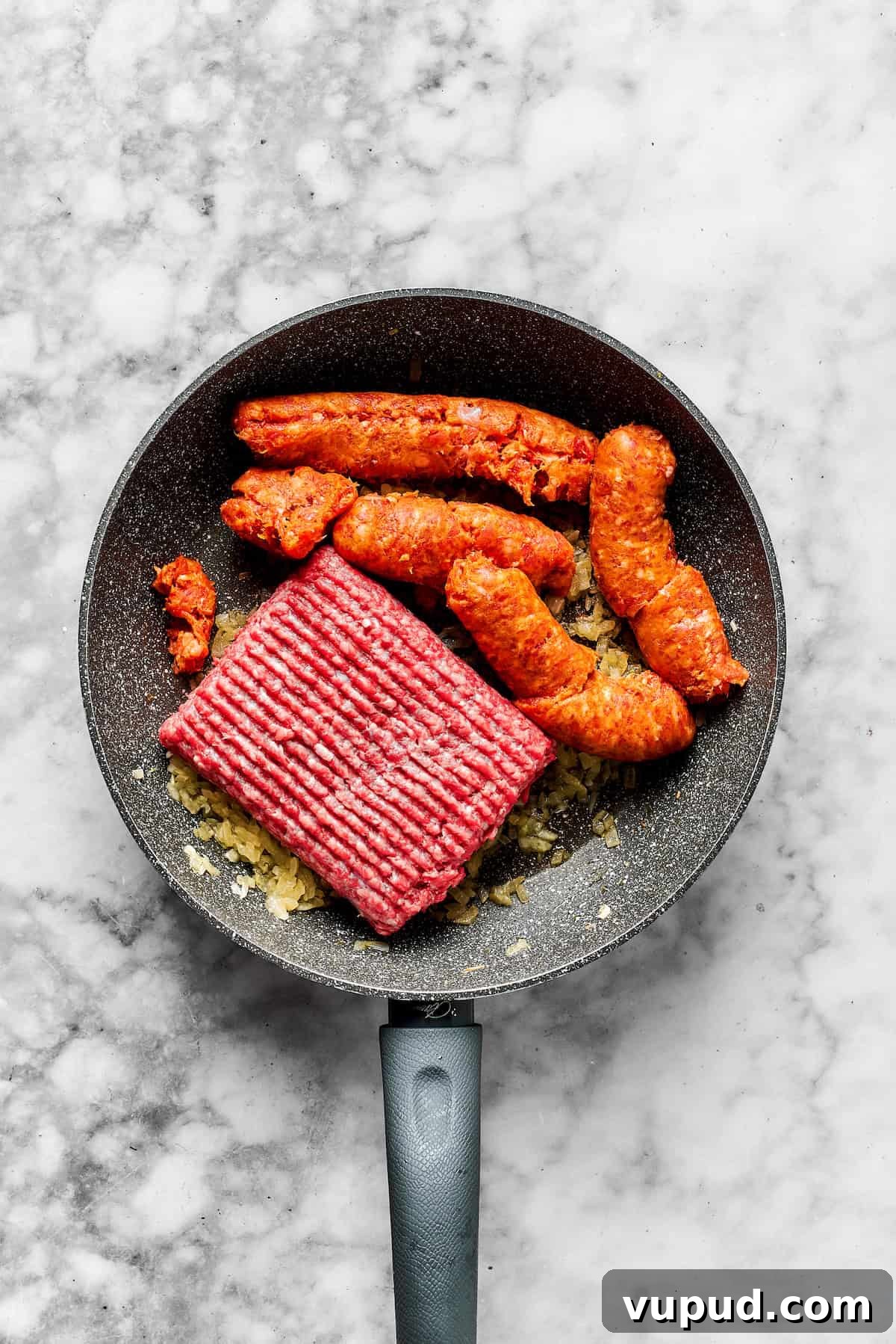 Break up the meat. Adding ground beef and sausage to the skillet.