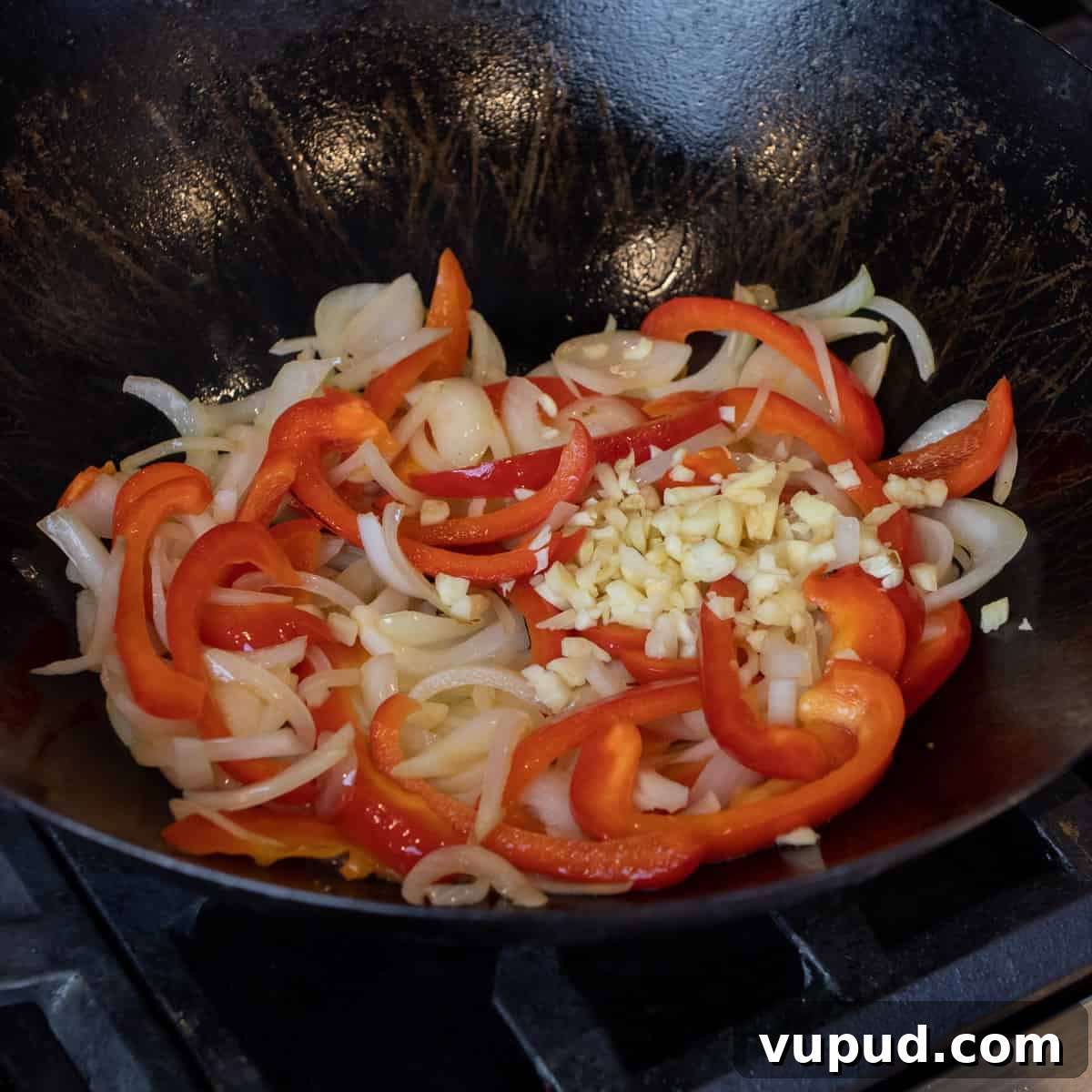 Vegetable Chow Mein Recipe: Flavorful Stir-Fry with Crunchy Veggies 4 Sliced onion and pepper with minced garlic sautéing in a wok.