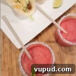 Two frozen watermelon margaritas with salt and lime on rim and tacos on plate