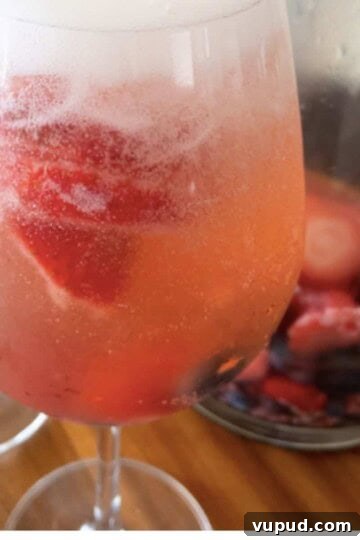 wine glass with summer sangria and pitcher in background with fresh berries and sangria