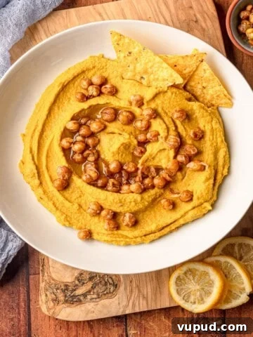 A white bowl filled with hummus that is topped with crispy chickpeas.