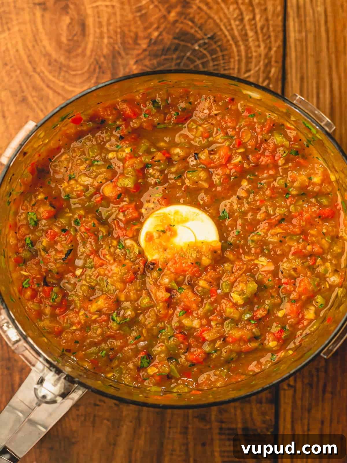 Smoky Roasted Tomato and Habanero Salsa Recipe 7 A food processor on a wooden surface filled with a blended salsa.