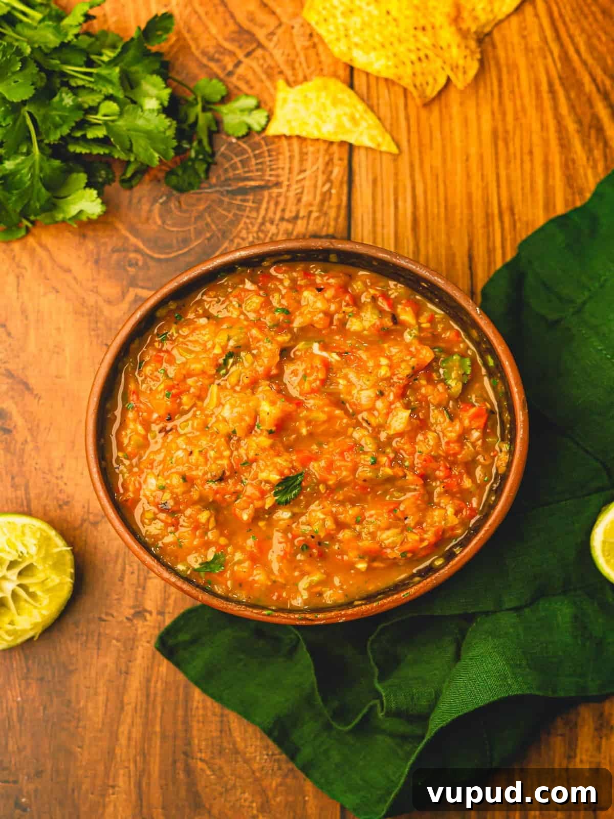 Smoky Roasted Tomato and Habanero Salsa Recipe 9 A wooden table topped with a bowl of salsa, green linen and cilantro.