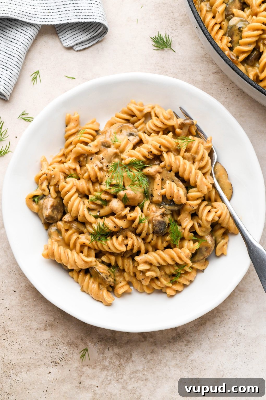 Cashew Cream Mushroom Stroganoff (Gluten-Free) 13 A white ceramic plate filled with creamy vegan mushroom stroganoff made with fusilli pasta and topped with fresh dill.