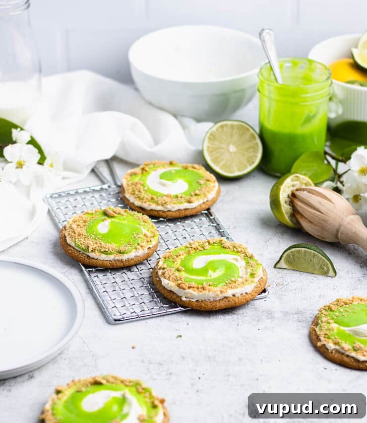 Zesty Key Lime Cookies Recipe: Tangy Citrus Cookie Delight 9 Three key lime cookies on a silver cooling rack next to a jar of lime curd, squeezed limes and an empty white plate.