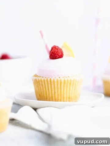 Close up of raspberry lemon cupcake on a plate with out of focus cupcakes around it.