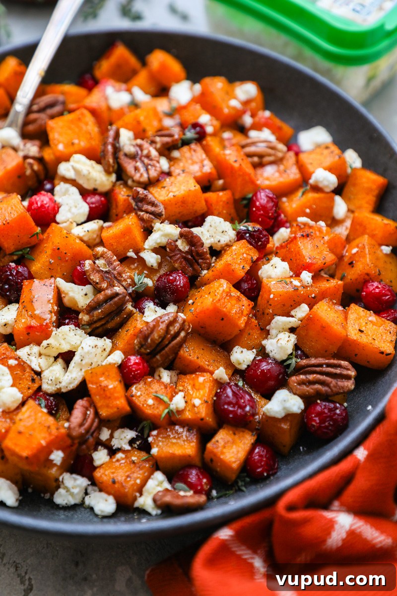Maple-Roasted Butternut Squash with Cranberries and Feta 2 A close up photo of maple roasted butternut squash topped with feta cheese, cranberries and toasted pecans