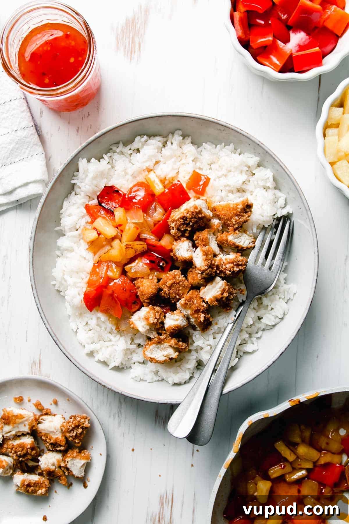 Gluten Free Panda Express Sweet Fire Chicken Copycat A shallow bowl filled with gluten-free sweet fire chicken atop a bed of rice. Two forks to the side along with remaining bell pepper, pineapple, and sweet chili sauce displayed around the bowl.
