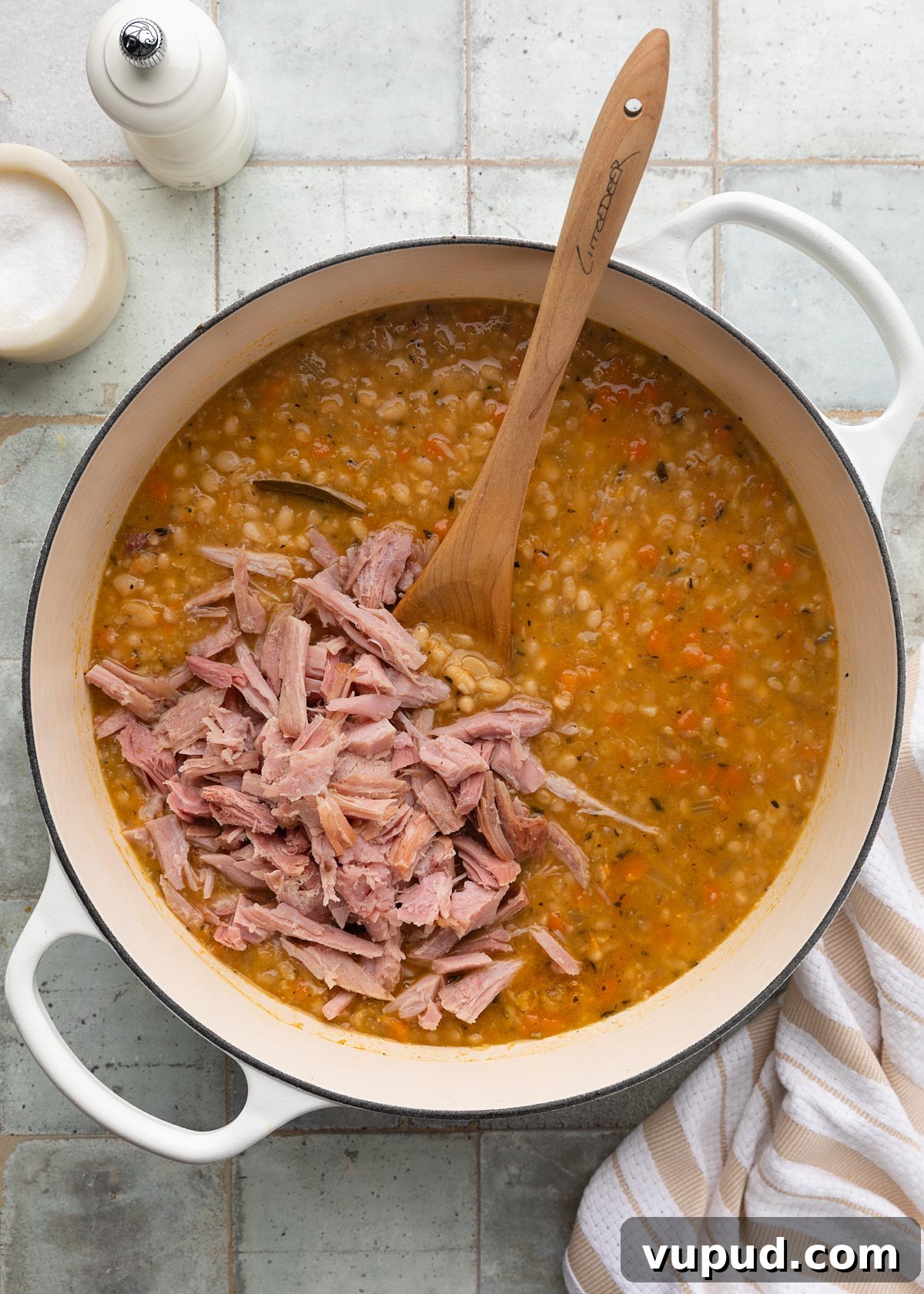 Classic Ham and Bean Soup Recipe for Comforting Weeknight Meals 11 shredded ham added to a pot of navy bean soup with a wooden spoon