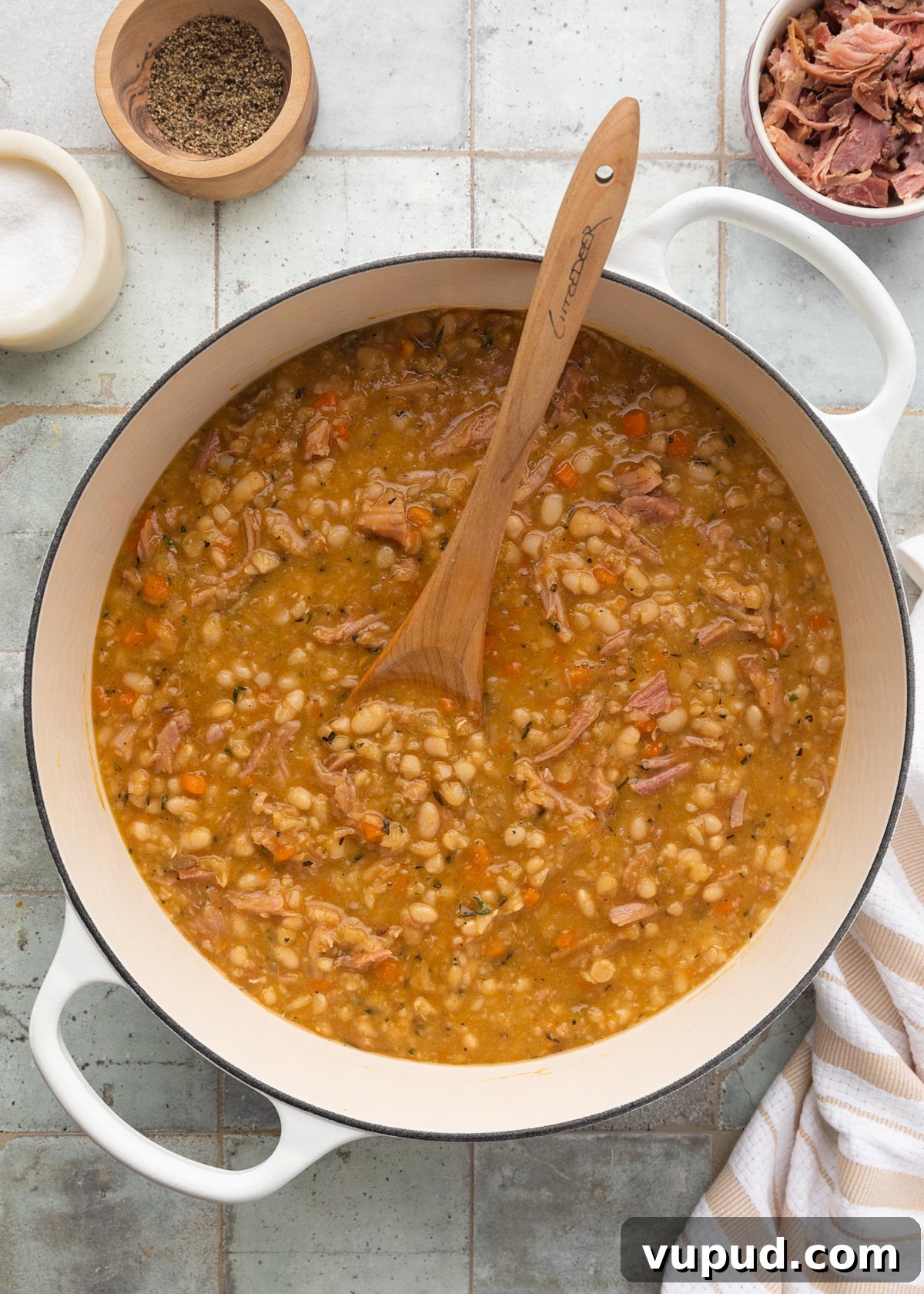 Classic Ham and Bean Soup Recipe for Comforting Weeknight Meals 12 cooked ham and navy bean soup in a white enameled cast iron Dutch oven with a wooden spoon