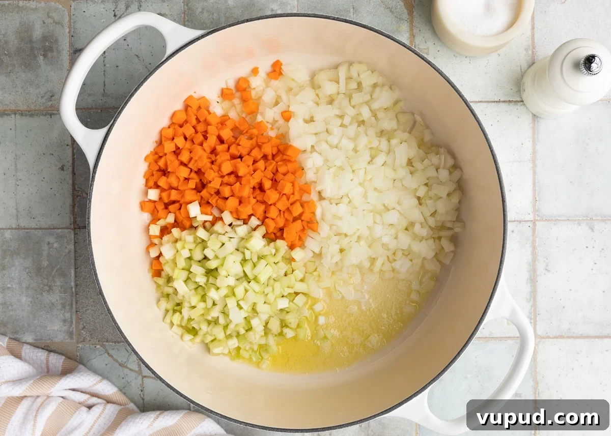 Classic Ham and Bean Soup Recipe for Comforting Weeknight Meals 6 diced celery, carrots, and onions with butter and olive oil in a white enameled cast iron Dutch oven