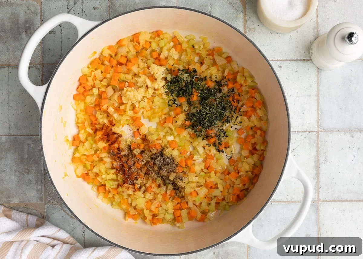 Classic Ham and Bean Soup Recipe for Comforting Weeknight Meals 7 sauteed mirepoix in a white enameled cast iron Dutch oven with fresh herbs, paprika, and black pepper added