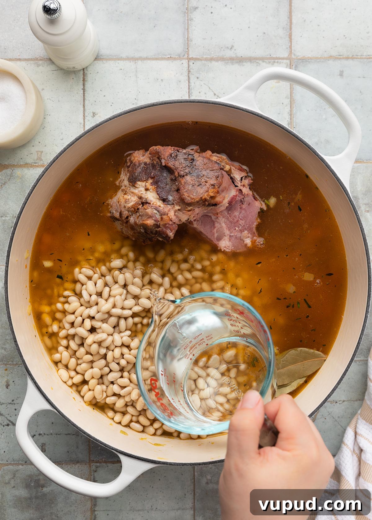 Classic Ham and Bean Soup Recipe for Comforting Weeknight Meals 9 water being poured from a liquid measuring cup into a white enameled cast iron Dutch oven with chicken stock, mirepoix, navy beans, and a ham bone