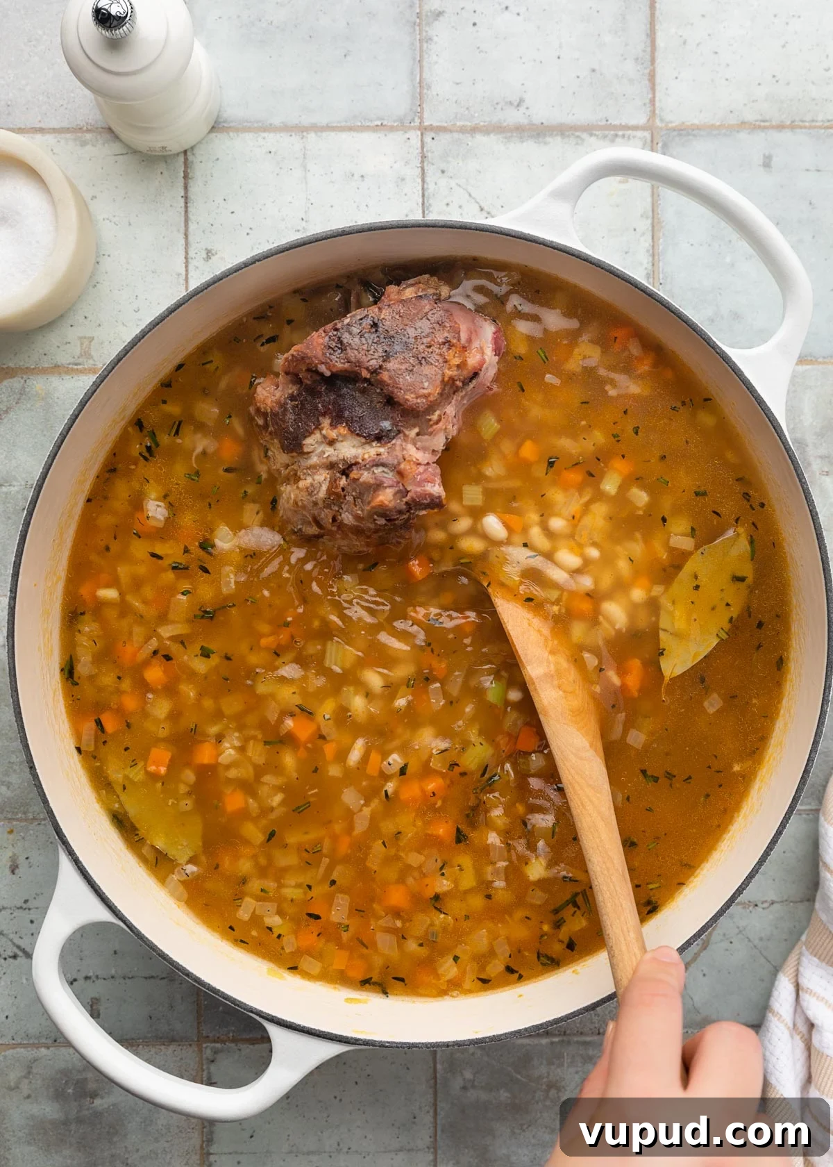 Classic Ham and Bean Soup Recipe for Comforting Weeknight Meals 10 stirring chicken stock and water into a pot of ham and bean soup with a wooden spoon