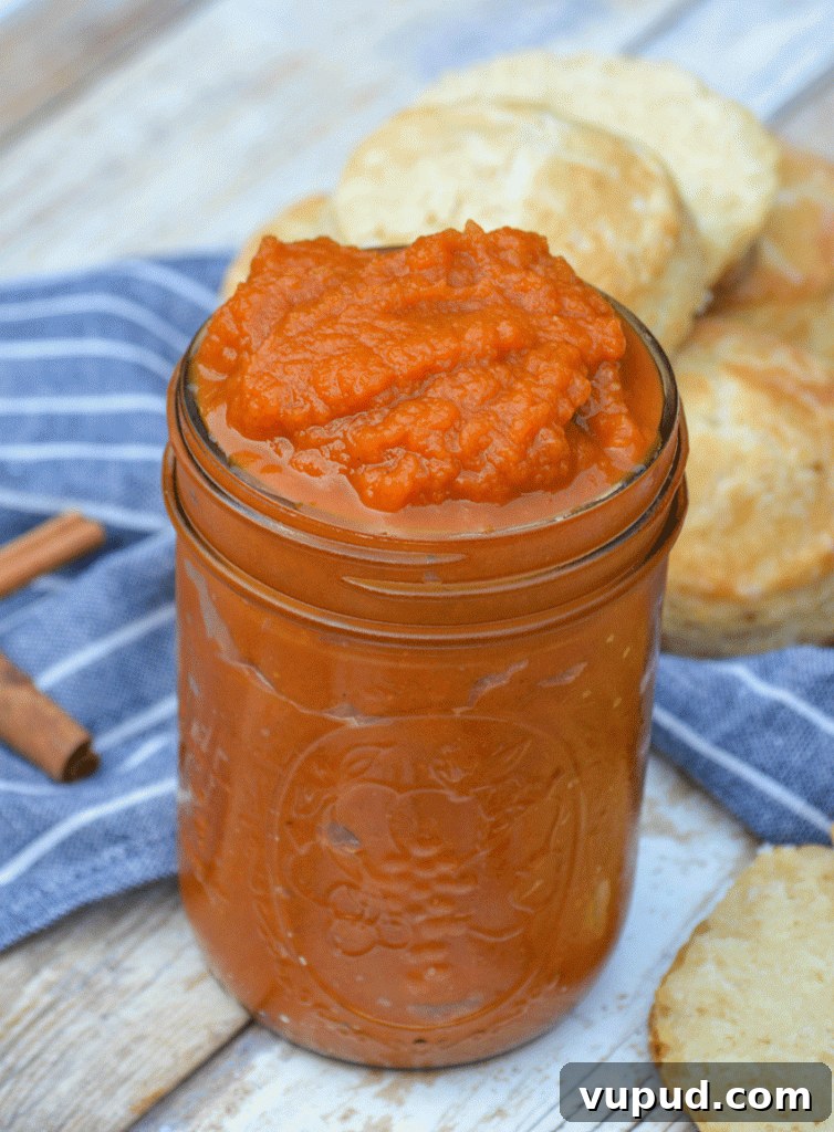instant pot pumpkin butter piled high in a glass mason jar surrounded by baked biscuits