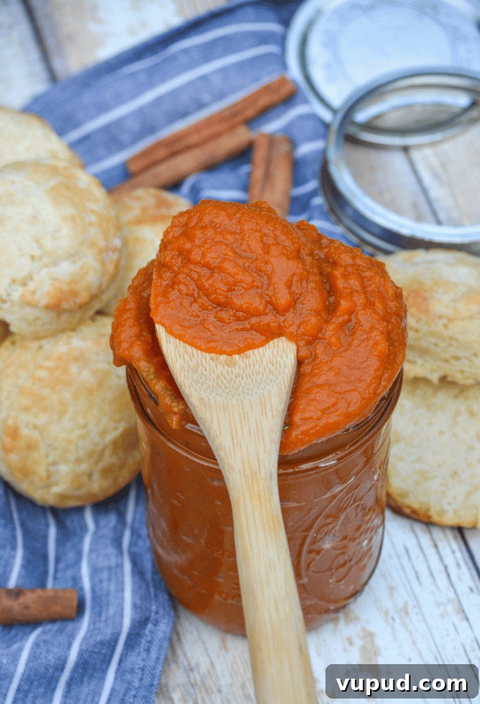 a wooden spoon covered in instant pot pumpkin butter resting on top of a jar filled with thick orange fruit butter