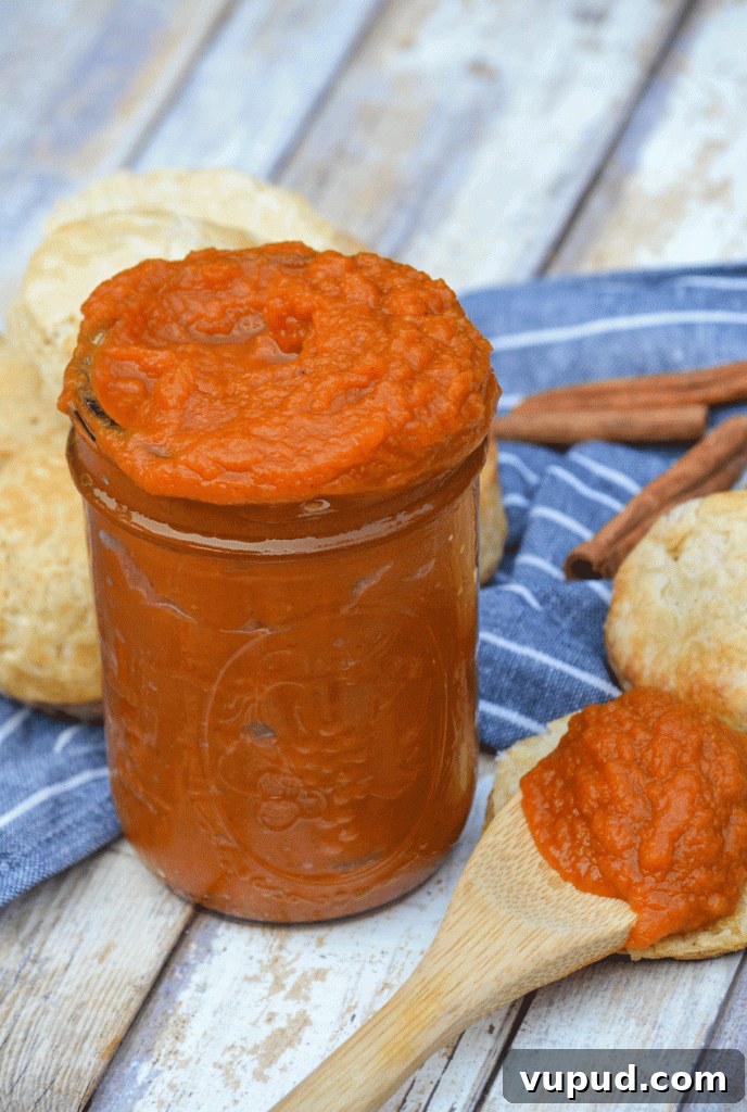 instant pot pumpkin butter piled high in a glass mason jar surrounded by baked biscuits
