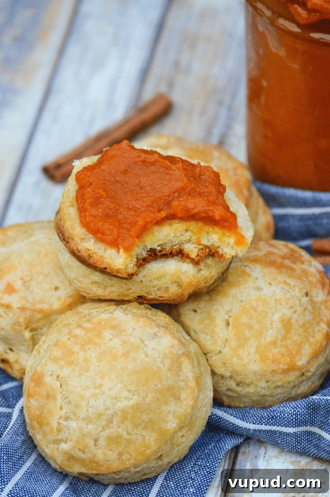 half of a buttermilk biscuit topped with instant pot pumpkin butter, resting on a pile of unopened biscuits