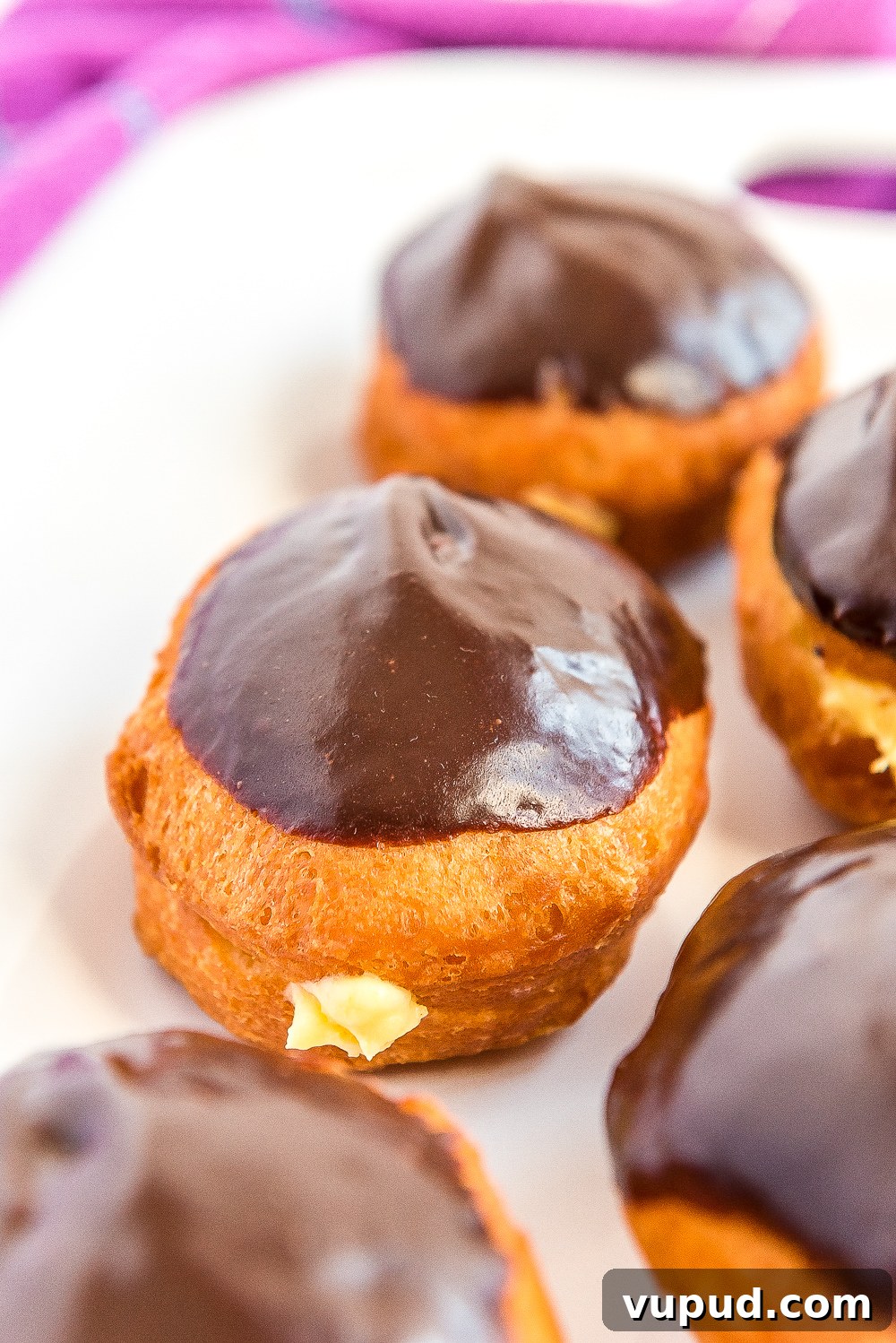 Boston Cream Donuts: Where to Find & How They're Made in Boston 11 Boston Cream Donuts on a white plate with a purple napkin.