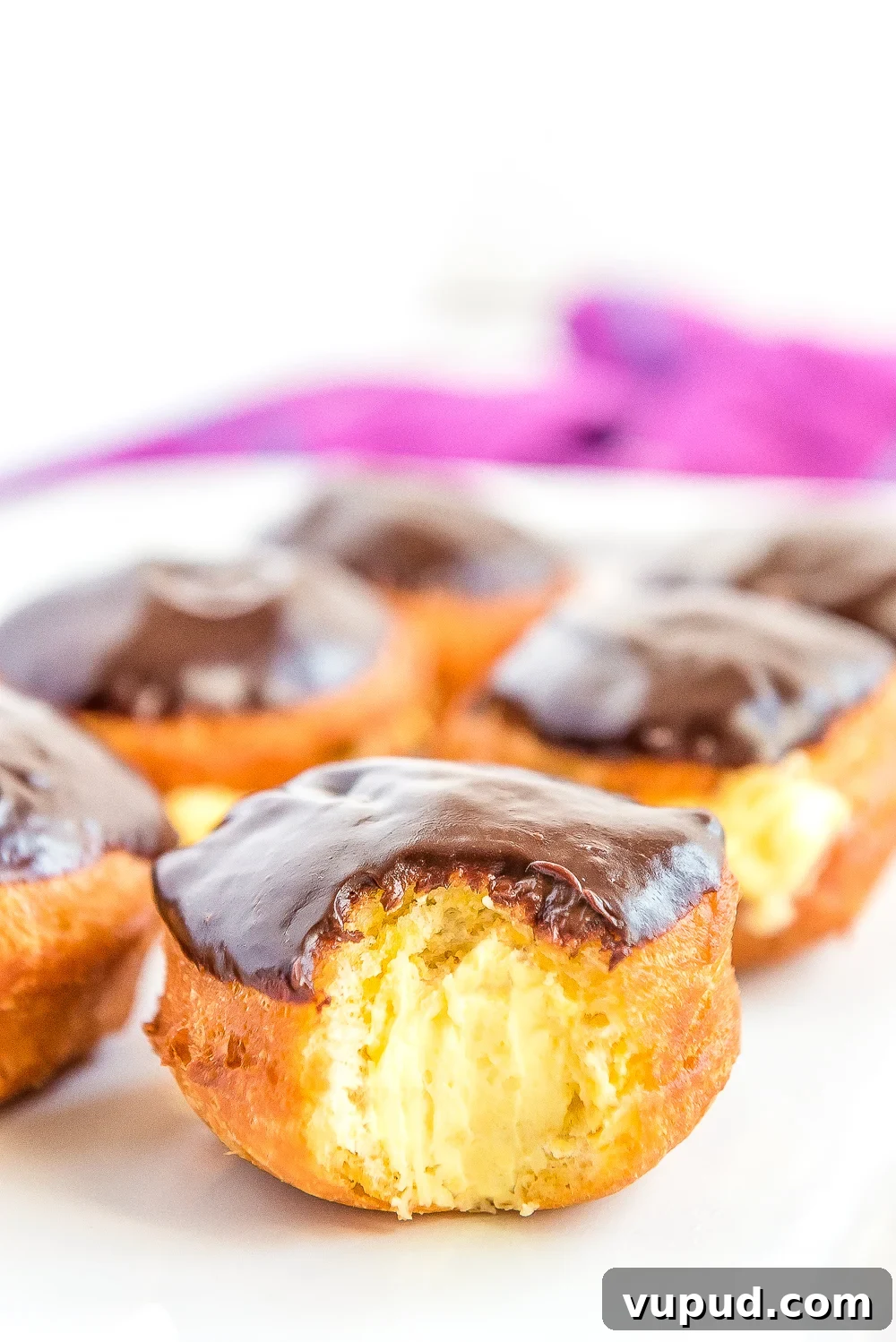 Boston Cream Donuts: Where to Find & How They're Made in Boston 12 Boston Cream Donuts on a white plate. One has a bite taken out of it.