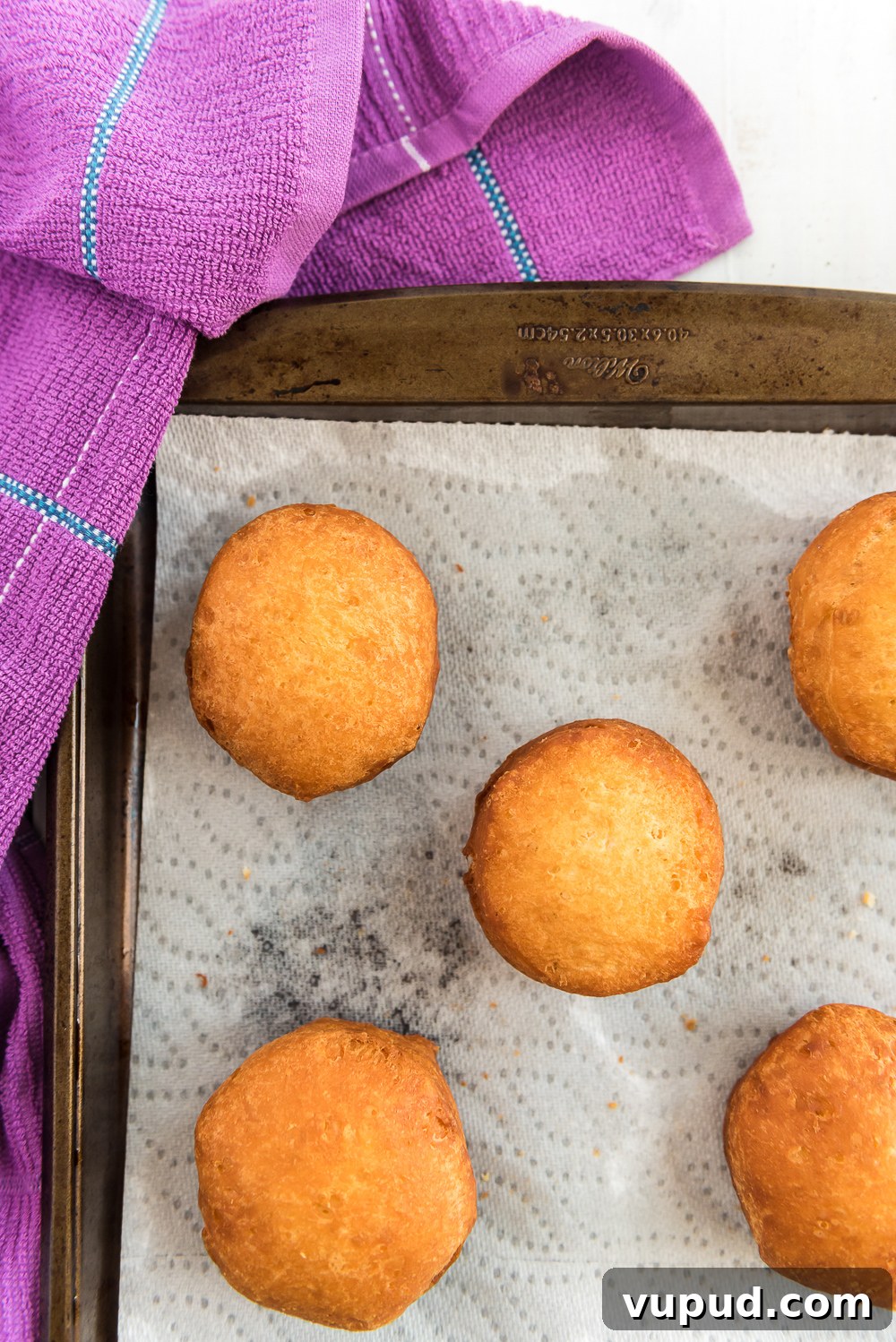 Boston Cream Donuts: Where to Find & How They're Made in Boston 5 Fried donuts on a paper towel-lined baking sheet with purple napkin.