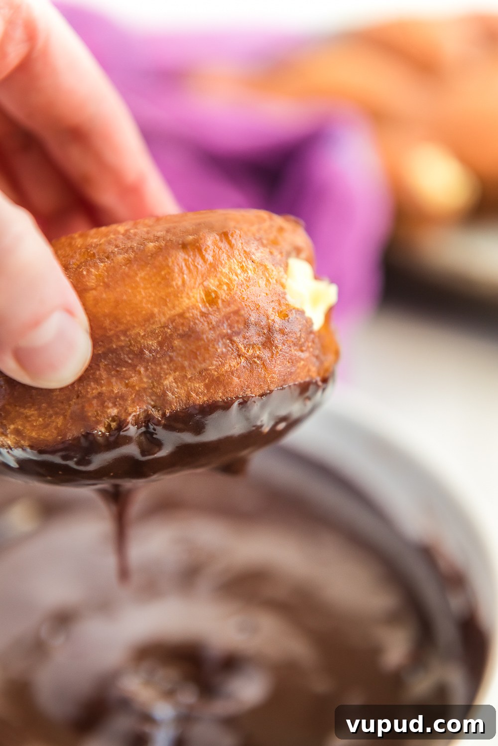 Boston Cream Donuts: Where to Find & How They're Made in Boston 10 Donut filled with pastry cream being dipped in chocolate ganache.