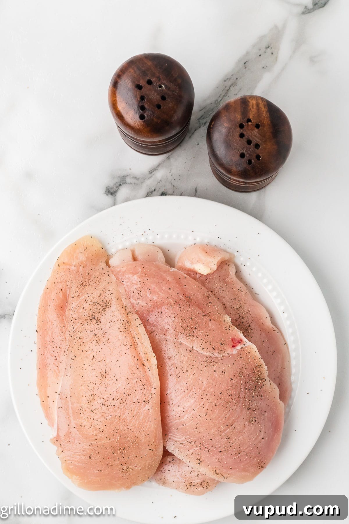 Crispy Pineapple Chicken on the Blackstone Grill: Sweet & Savory Recipe 5 Uncooked chicken breast on a plate seasoned with salt and pepper