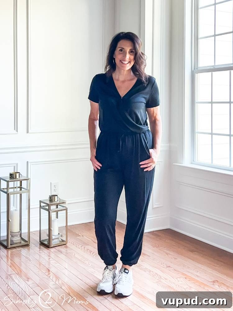blogger standing inside wearing black one piece jumpsuit with hands in pockets