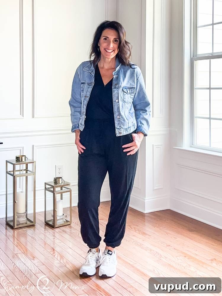 blogger standing inside wearing black one piece jumpsuit with cinched ankles with jean jacket and sneakers