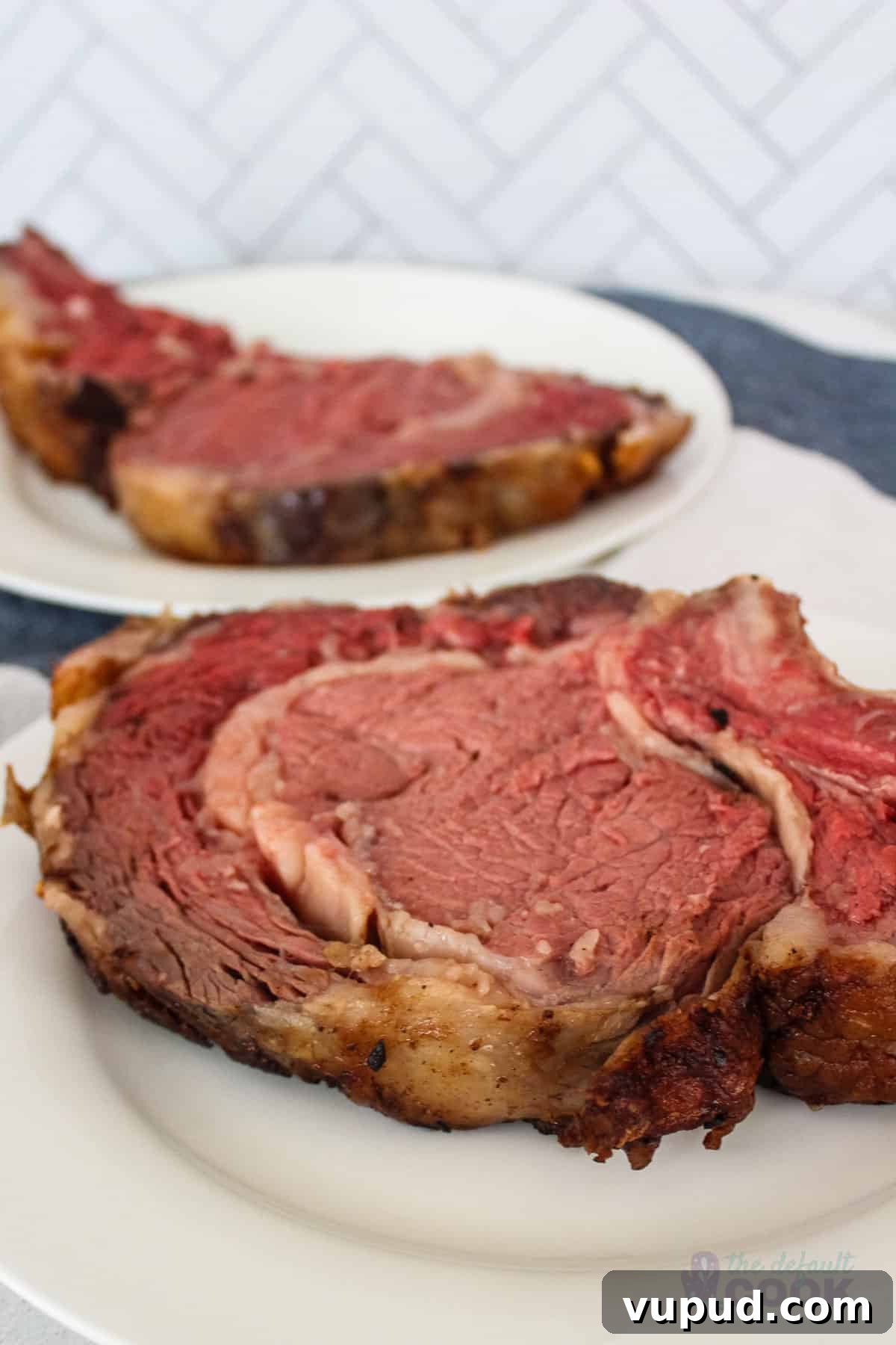 Perfectly Tender Sous Vide Prime Rib Roast Recipe 2 Two plates with oversized slices of prime rib on them on a kitchen towel.